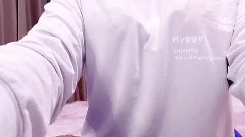 Media: A video of a person wearing a white long-sleeve shirt, with text reading \"Hygge\" and \"enjoying my little moment.\" The background features a pink blanket and beige curtains.