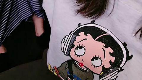 Media: Video of a person wearing a white t-shirt with a cartoon astronaut character, large eyes, and a red nose, against a striped shirt.