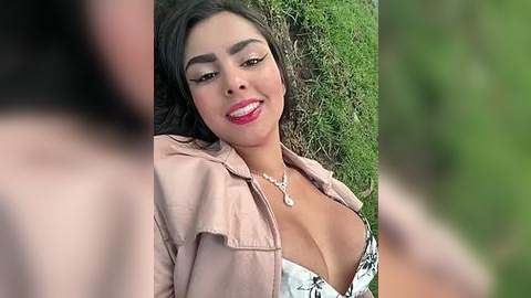 Media: Video of a smiling, Latina woman with dark hair, wearing a pink jacket and revealing black floral top, lying on grass.