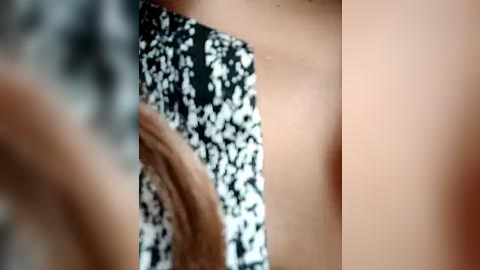 Media: Video of a close-up of a person\u2019s bare upper chest, showing light skin and a black and white floral patterned shirt, with blurred out faces in the background.