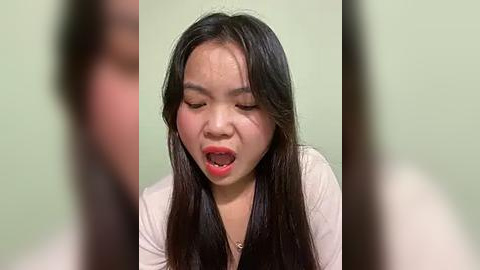 Media: Video of an Asian woman with long black hair, wearing a white top, mouth open in a scream, against a green background.