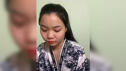 Media: A video of a young East Asian woman with long black hair, wearing a patterned robe with black and white abstract designs, and red lipstick, against a light green background.