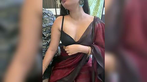 Media: A video of a South Asian woman in a black and burgundy sari, with a sheer blouse, against a background of patterned fabrics.