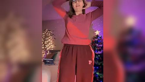 Media: A video of a woman in a red sweatshirt and pants, dancing in front of a Christmas tree adorned with ornaments and lights, in a warmly lit room.