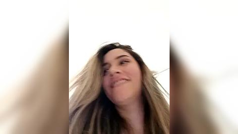 Media: Video of a smiling woman with long, wavy brown hair, captured from a low angle, creating a dynamic, playful perspective.