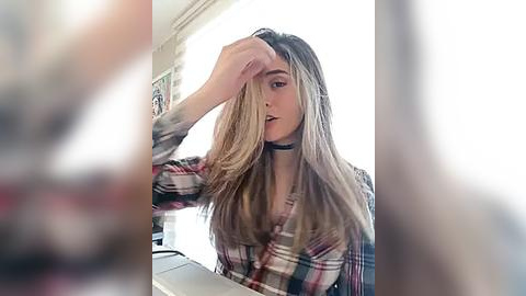 Media: Video of a young woman with long, blonde hair, wearing a plaid shirt, black choker, and a serious expression, adjusting her hair.