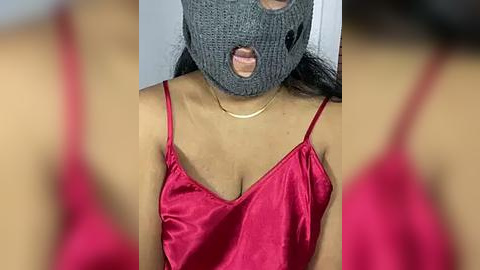 Media: A close-up video shows a woman with medium skin tone wearing a gray knit mask and a red satin camisole, lips slightly parted.