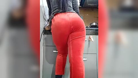 Media: Video of a person's lower back and buttocks in tight red pants, standing in a modern kitchen with gray cabinets and a countertop.