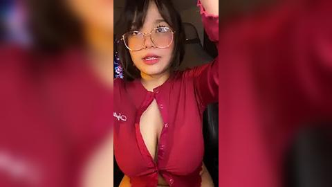 Media: A video of a young Asian woman with a medium build and medium-sized breasts, wearing a red blouse with a low neckline, taking a selfie in a car.