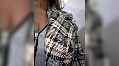 Media: A video of a woman in a close-up, cropped view, wearing a black and white plaid jacket over a grey top, with blurred background.