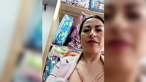 Media: A video of a smiling, light-skinned woman with dark hair, wearing a pink shirt, standing in a grocery store aisle with colorful packaged goods.