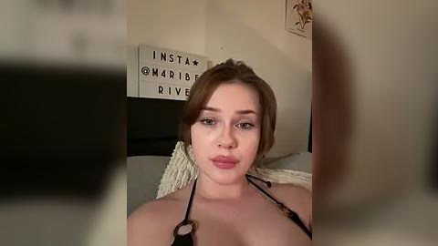 Media: A video of a fair-skinned, red-haired woman in a black bra, with a stethoscope around her neck, in a dimly lit bedroom with a white wall and framed art.