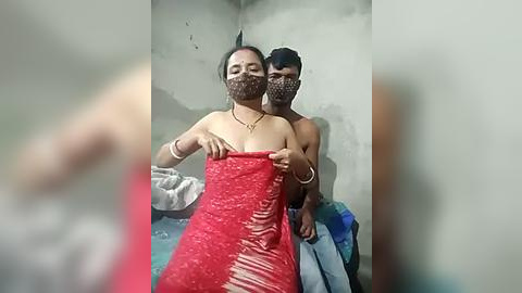 Media: A video shows a shirtless man and a woman with a red, torn dress in a dimly lit, run-down room with peeling walls. Both wear masks, and the woman holds a blue towel.