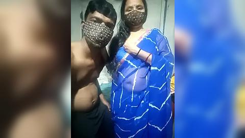 Media: Video of two people, one shirtless and wearing a face mask, the other in a blue sari with a white pattern, both standing indoors.