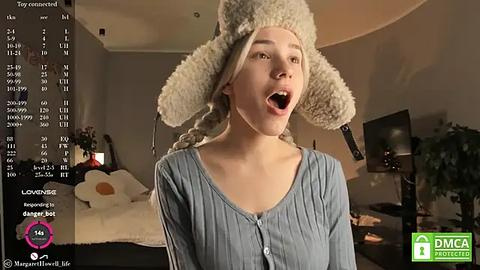 Media: Video of a young woman with a large, fluffy sheep hat, mouth open, standing in a dimly lit living room with a TV and plant in the background.