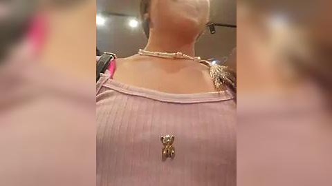 Media: A video of a woman wearing a light pink ribbed tank top with a gold bee pendant, a pearl necklace, and a black crossbody bag.