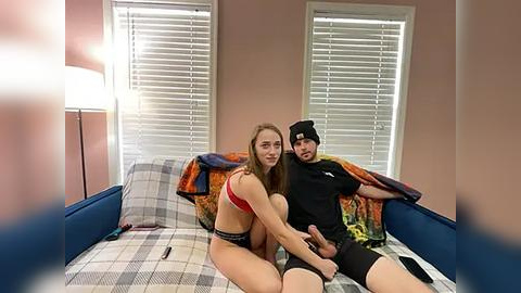 Media: A video of a young woman in a red bra and black panties, sitting on a bed with a man in a black hoodie and headband.