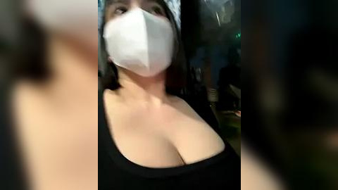 Media: A blurry video of a woman with a white mask, black top, and long dark hair, standing indoors, possibly in a park.