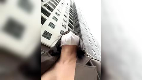 Media: Video of a woman in a white mask, walking down a narrow alley between tall, modern buildings, blurred in the foreground.