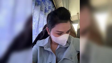 Media: A video of an Asian woman in a light blue shirt with a white mask, looking down, in a dimly lit airplane cabin.