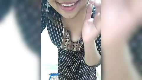 Media: A close-up video of a smiling woman in a black patterned dress with a gold necklace, partially obscured by a blurred figure in the foreground.
