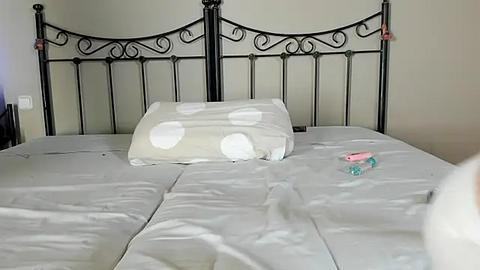 Media: A video of a neatly made bed with a black wrought iron headboard, white sheets, and a white pillow with large pink polka dots. A pink toy is placed on the pillow.