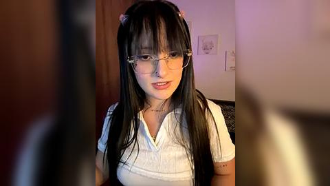 Media: A video of a young woman with long black hair, wearing glasses and a white blouse, standing in a dimly lit room with a blurred background.