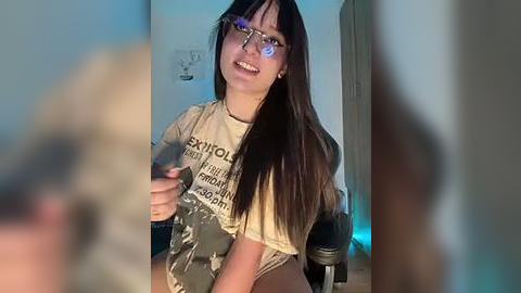 Media: A video of a young woman with long dark hair, glasses, and a t-shirt, sitting in a dimly lit room with blurry background.