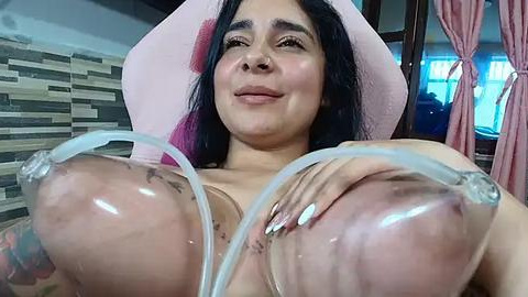 Media: Video of a Latina woman with long black hair, wearing a pink hat, lying back, exposing large, glistening breasts, nipples visible, in a tiled room with a window.