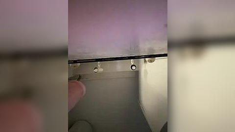 Media: A video of a ceiling-mounted toilet paper holder, featuring three metal arms holding rolls of toilet paper, with a blurred background and a hand holding a roll.