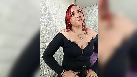 Media: A video of a plus-size woman with bright red hair, wearing a black off-shoulder top, standing against a white brick wall. Her breasts are large, and she has a confident expression.