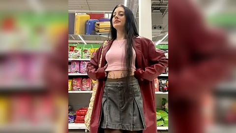 Media: Video of a confident woman with long black hair, wearing a pink crop top, gray pleated skirt, and red jacket, standing in a brightly lit toy store with colorful shelves and boxes in the background.