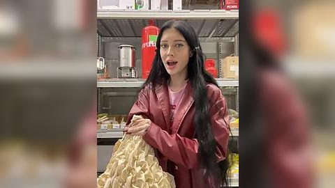 Media: A video of a young Asian woman with long black hair, wearing a maroon jacket, holding a beige bag in a supermarket aisle with red soda bottles and a coffee maker in the background.