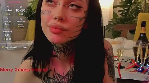 Media: Video of a woman with black hair and tattoos, wearing a black top, smiling and making a kissy face, surrounded by a messy table with drinks and confetti.