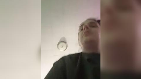 Media: A blurry video of a person in a black robe, possibly a surgeon or medical professional, with a lit ceiling light visible in the background.