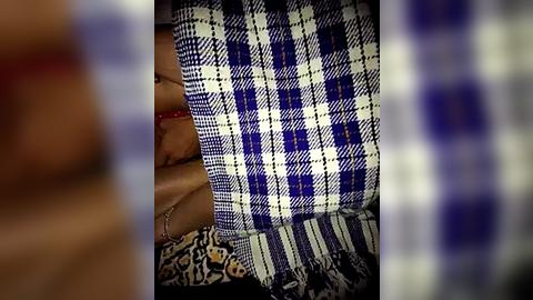 Media: Video of a person lying on a blue and white plaid blanket, partially covered by a patterned fabric. The image is slightly blurred, focusing on the textures and colors of the textiles.
