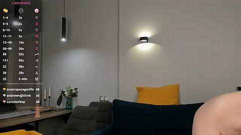 Media: Video of a modern living room with a dark couch, yellow pillows, and a white wall featuring a single light fixture. A smartphone screen with a camera view and social media icons is visible.