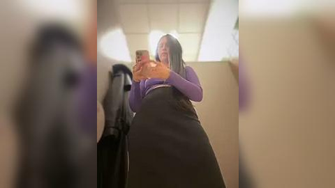 Media: Video of a woman with long gray hair, wearing a purple top and black skirt, holding a baby in a stroller, in a dimly lit, beige-walled hallway.