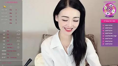 Media: A video of a young Asian woman with long black hair, fair skin, and red lipstick, smiling, wearing a white button-up shirt. She sits on a beige sofa with a purple backdrop featuring a tarot card reading.