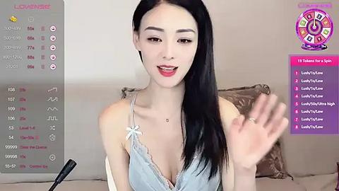 Media: Video of a smiling Asian woman with long black hair, wearing a lacy bra, on a beige couch.