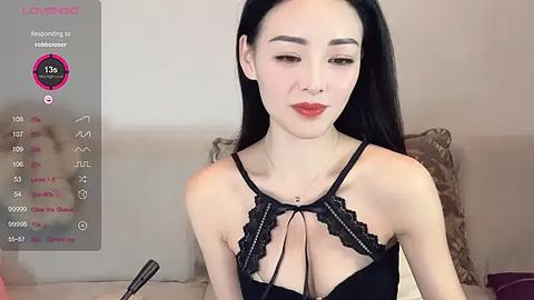 Media: Video of an Asian woman with long black hair, wearing black lace lingerie, sitting on a beige sofa. She has a slim physique, fair skin, and red lipstick.