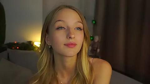 Media: Video of a young, fair-skinned, blonde woman with blue eyes, wearing a simple top, indoors with dim lighting, a fireplace, and Christmas decorations in the background.