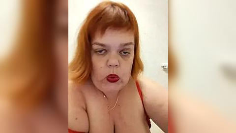 Media: Video of a plus-size woman with red hair and fair skin, wearing a red spaghetti strap top, making a pouty face, blurred in the foreground.