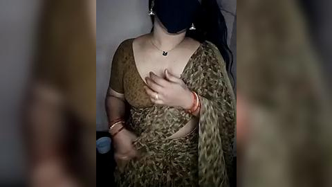 Media: Video of a woman in traditional Indian attire, wearing a mask, holding her chest, with a blurred background.