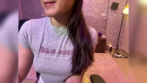 Media: A video of a young woman with medium skin tone, long dark hair, and wearing a San Jose State Athletics t-shirt, seated in a dimly-lit room with purple wallpaper and a floor lamp.