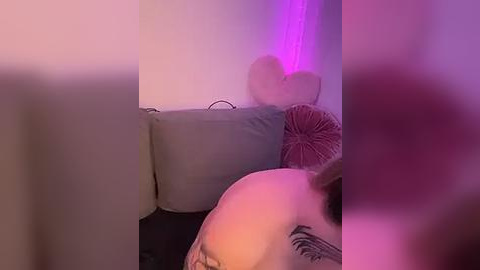 Media: A video of a person with a tattoo on their back, lying on a gray couch with pink and purple lights illuminating the room.