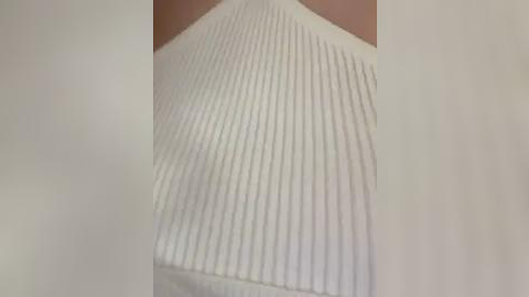 Media: Video of a white, ribbed fabric, likely a piece of clothing, with a textured, ridged pattern. The background is blurred, focusing on the fabric's detailed texture.