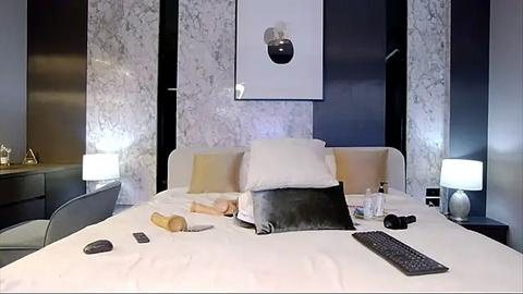 Media: Video of a modern bedroom with a white bed, black marble walls, minimalist decor, two bedside lamps, and a laptop on the bed.