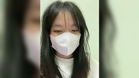 Media: Video of a young Asian girl with long black hair, wearing a white surgical mask and a white shirt, against a blurred background.