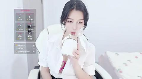 Media: Video of an Asian woman with dark hair, wearing a white blouse, sucking on a lollipop. Background features a white bed with floral pillows.